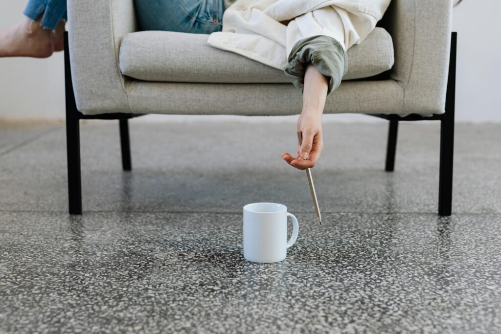 A person casually relaxes on a sofa, reaching for a ceramic mug using a pencil.